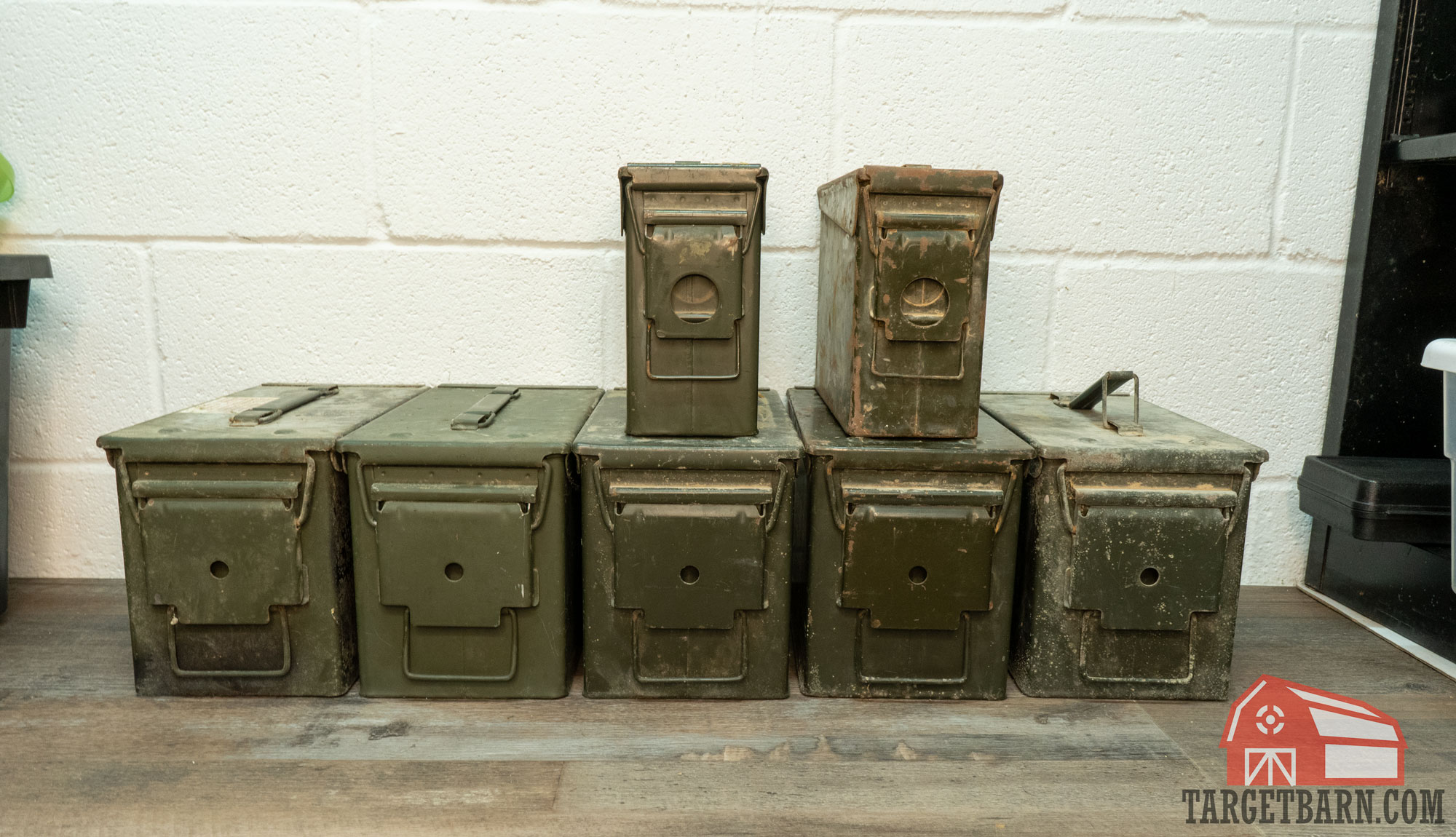 five 50 cal ammo cans and two 30 cal ammo cans stacked against a wall