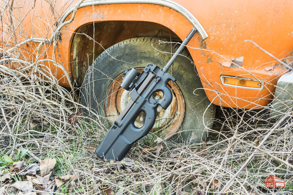 an fn ps90 with optic leaning against and old orange truck